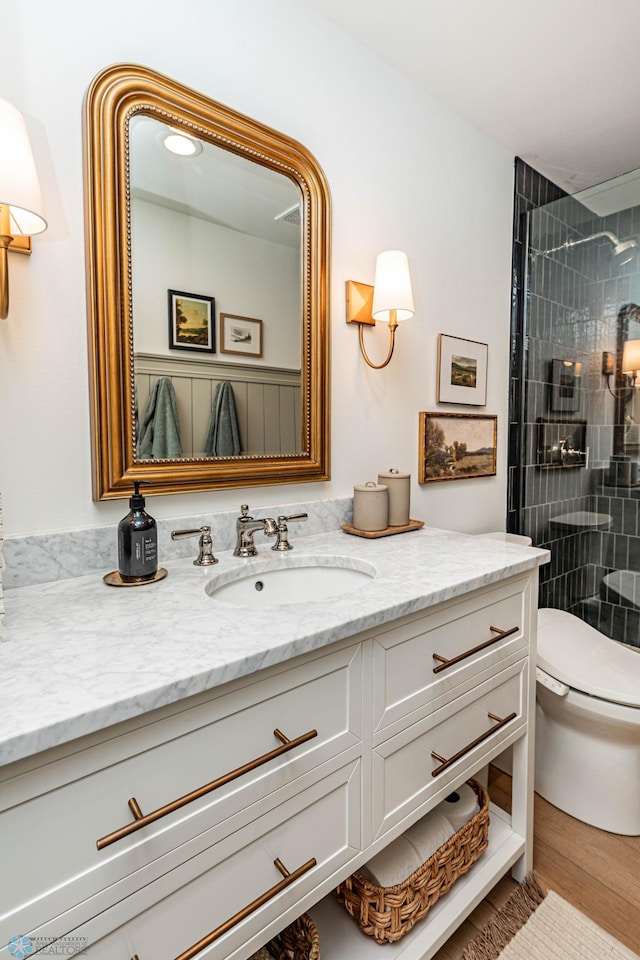 bathroom with hardwood / wood-style floors, tiled shower, vanity, and toilet