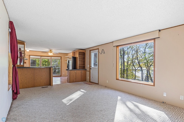 unfurnished living room with ceiling fan, light colored carpet, and a textured ceiling