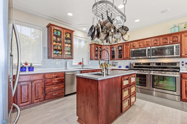 kitchen with backsplash, appliances with stainless steel finishes, light wood-type flooring, and a kitchen island with sink