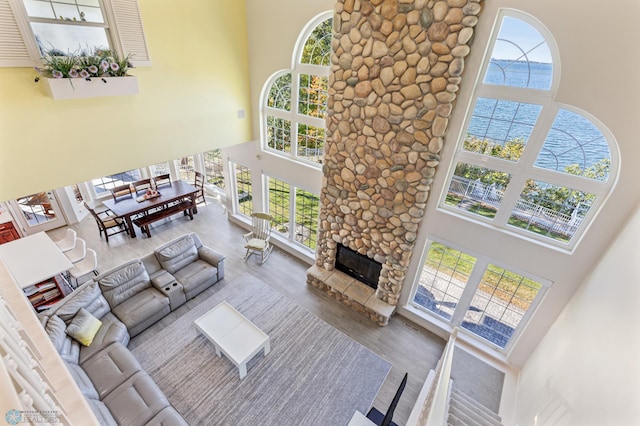 living room with a wealth of natural light, a high ceiling, a stone fireplace, and a water view