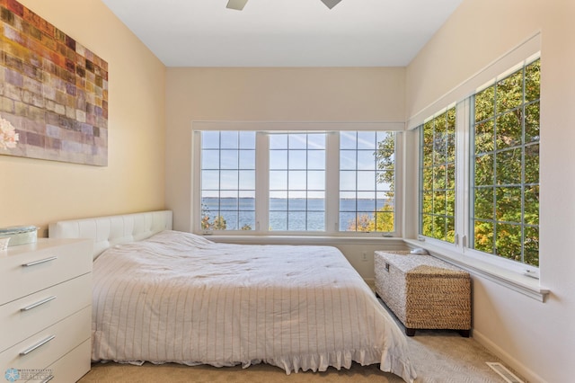 carpeted bedroom featuring multiple windows, a water view, and ceiling fan