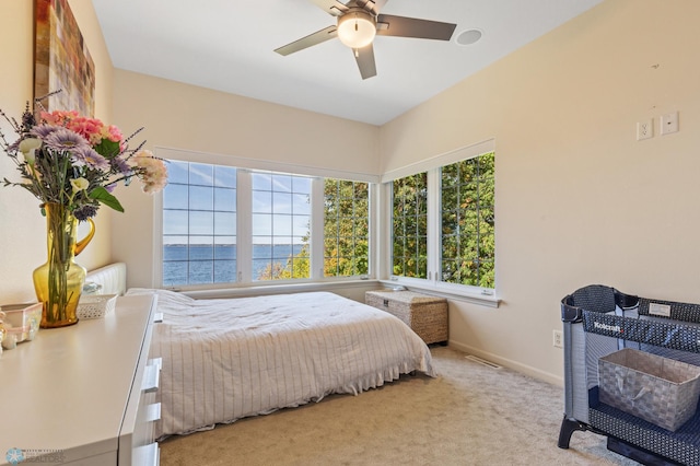 carpeted bedroom featuring a water view and ceiling fan