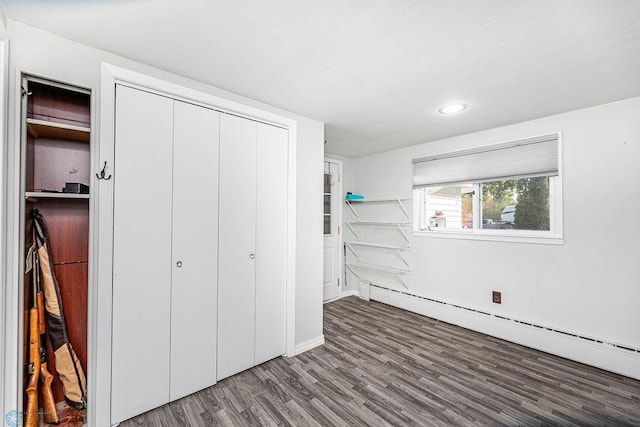 unfurnished bedroom featuring baseboard heating, dark wood-type flooring, and a closet