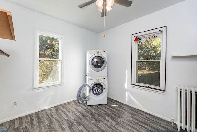 clothes washing area featuring radiator, stacked washer / dryer, dark hardwood / wood-style flooring, and a wealth of natural light