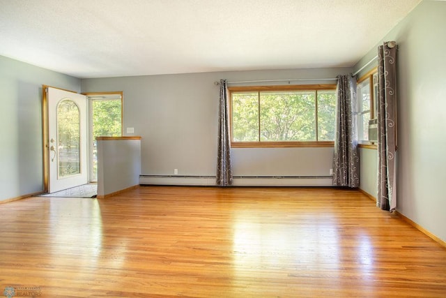 empty room with baseboard heating, light hardwood / wood-style flooring, and a wealth of natural light