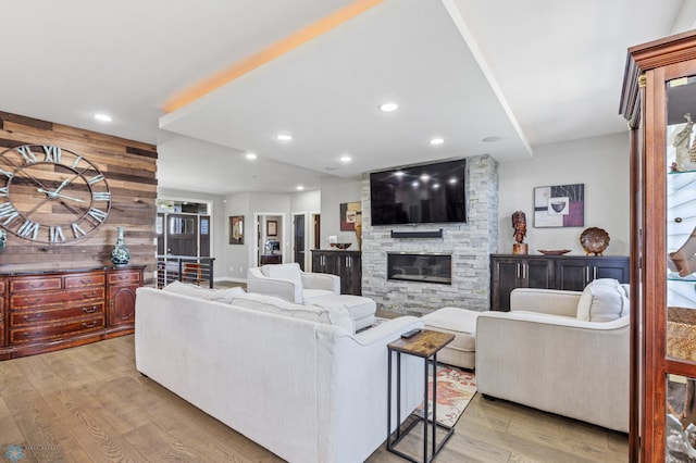 living room with a stone fireplace, wooden walls, and light hardwood / wood-style flooring