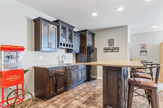 kitchen featuring dark brown cabinetry, sink, black refrigerator, and a kitchen breakfast bar