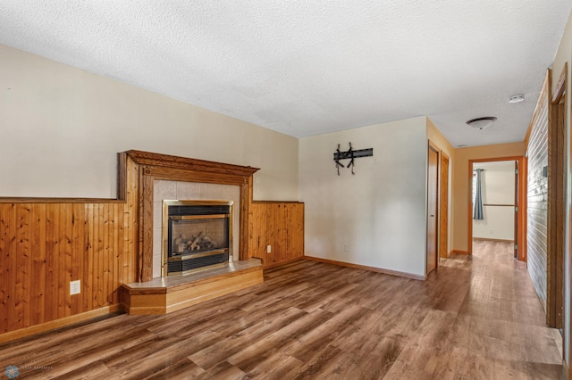 unfurnished living room featuring wood-type flooring, wooden walls, a textured ceiling, and a tile fireplace