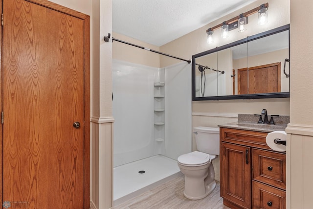 bathroom with walk in shower, toilet, hardwood / wood-style floors, vanity, and a textured ceiling