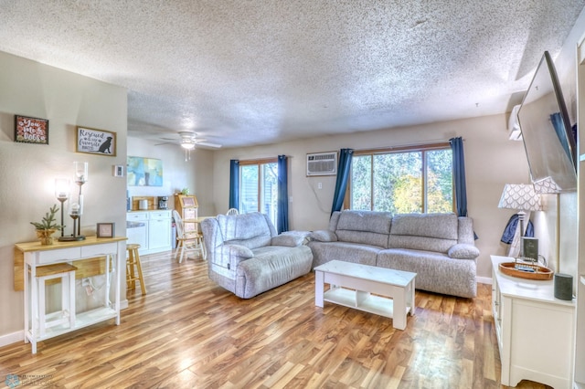 living room with ceiling fan, a textured ceiling, light hardwood / wood-style flooring, and a wall mounted air conditioner