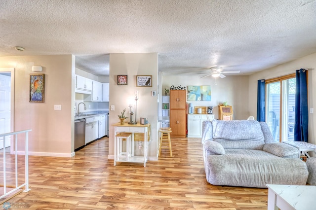 living room with light wood-type flooring, ceiling fan, sink, and a textured ceiling