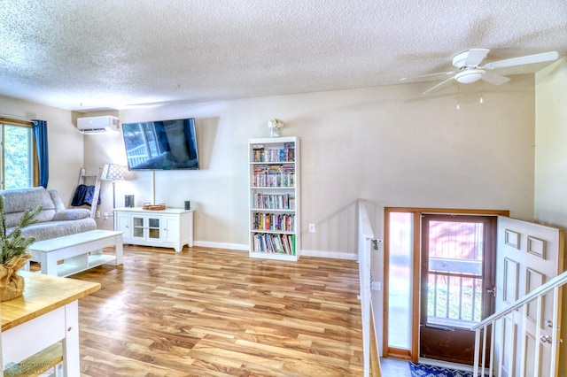 living room featuring a textured ceiling, an AC wall unit, light wood-type flooring, and ceiling fan