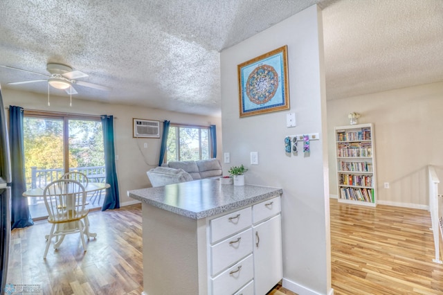 kitchen with light hardwood / wood-style floors, a wall unit AC, kitchen peninsula, white cabinets, and a textured ceiling