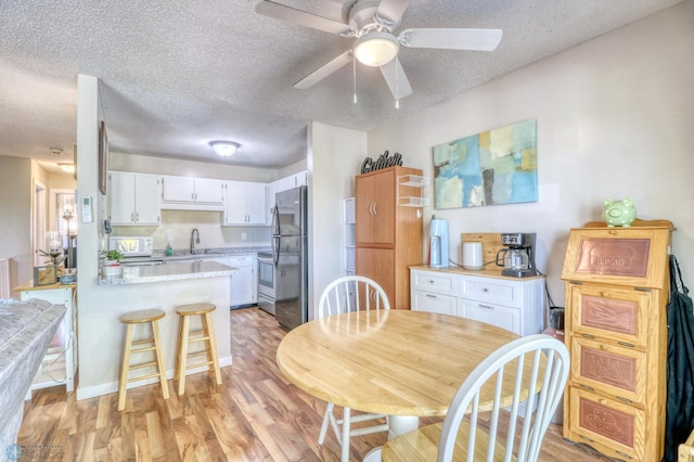 dining room featuring ceiling fan, sink, light wood-type flooring, and a textured ceiling