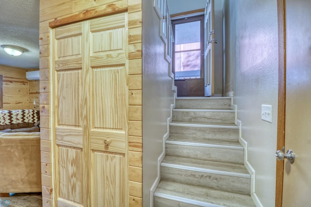 staircase with wooden walls and a textured ceiling