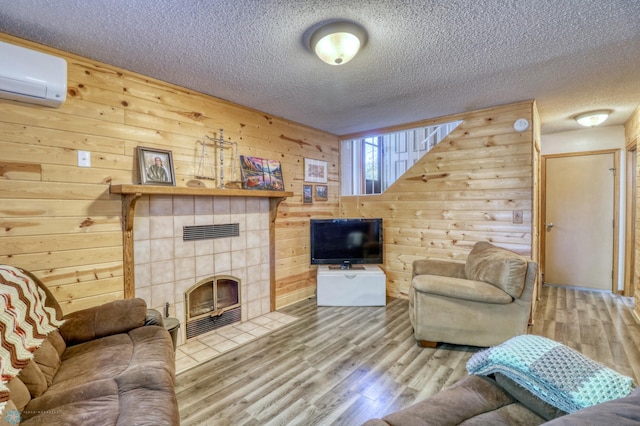 living room featuring wooden walls, a tile fireplace, hardwood / wood-style floors, and a textured ceiling