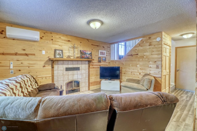 living room with wood walls, a wall unit AC, light wood-type flooring, a fireplace, and a textured ceiling