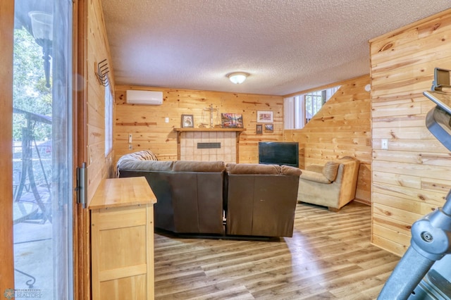 living room with light wood-type flooring, a wall unit AC, wooden walls, and a textured ceiling