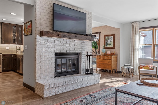 living room with a brick fireplace, light hardwood / wood-style floors, and sink