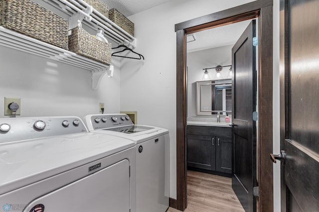 clothes washing area with washing machine and clothes dryer, sink, light wood-type flooring, and a textured ceiling