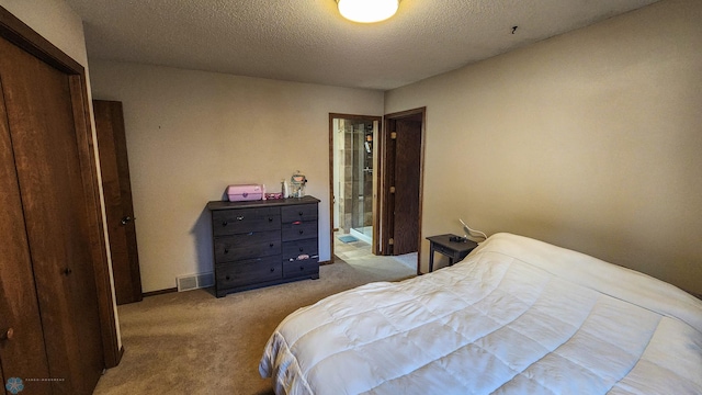 carpeted bedroom featuring a closet, ensuite bath, and a textured ceiling