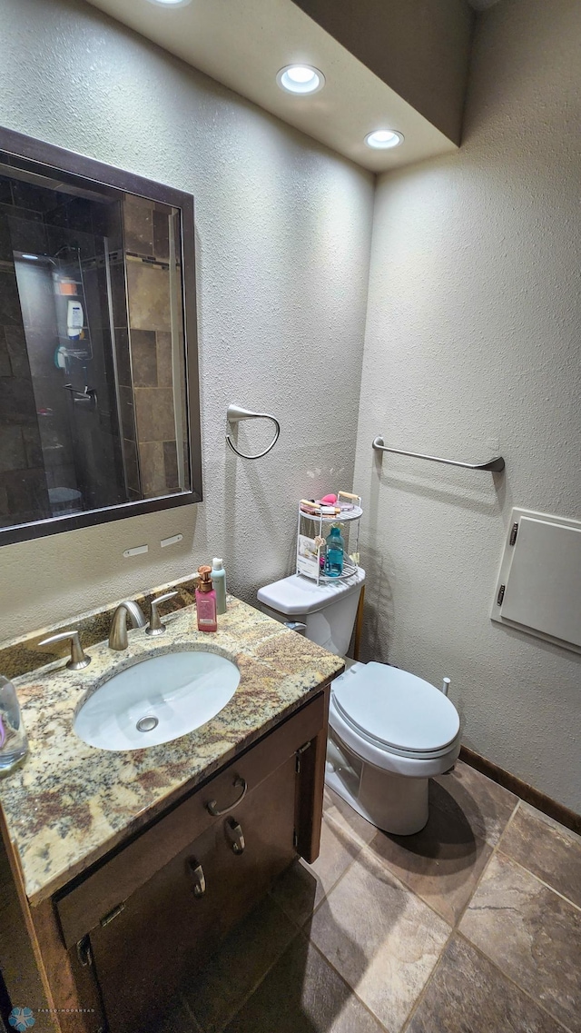 bathroom featuring vanity, a tile shower, and toilet