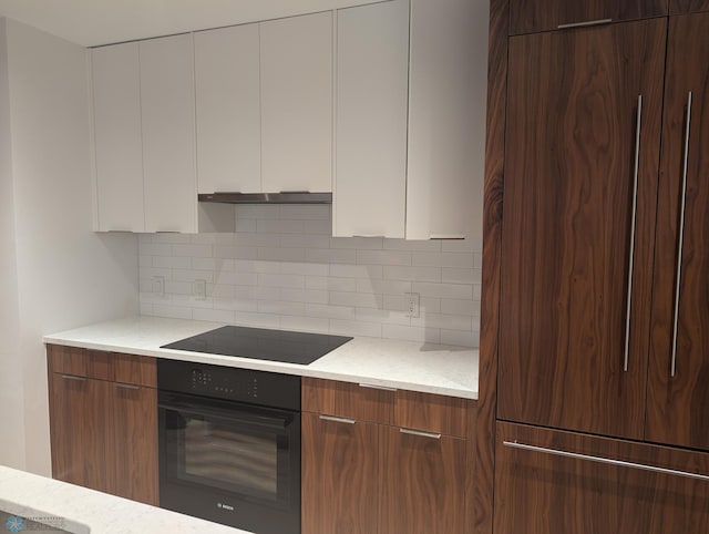 kitchen featuring light stone countertops, backsplash, white cabinets, and black appliances