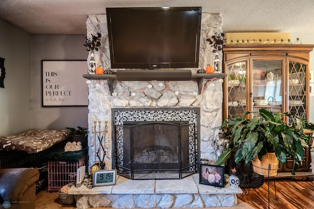 interior details featuring wood-type flooring, a stone fireplace, and a textured ceiling