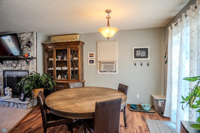 dining area with hardwood / wood-style flooring, cooling unit, a stone fireplace, and a textured ceiling