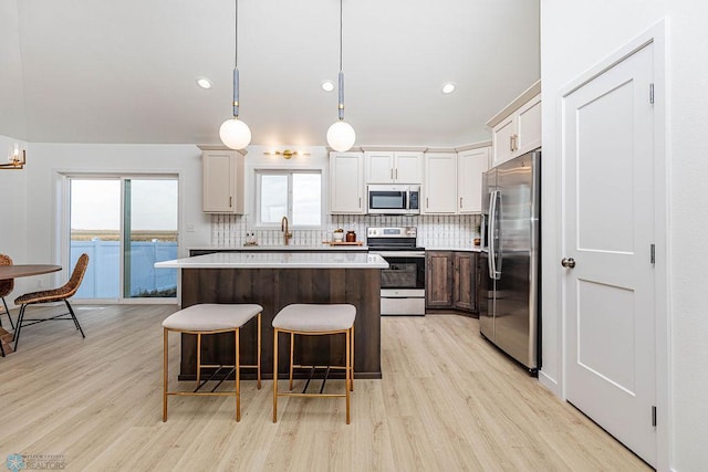 kitchen with decorative light fixtures, light hardwood / wood-style flooring, stainless steel appliances, a center island, and a water view