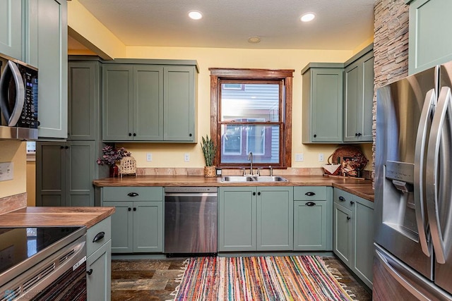 kitchen with stainless steel appliances, wooden counters, sink, green cabinets, and a textured ceiling