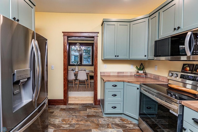 kitchen featuring dark wood-type flooring, butcher block countertops, appliances with stainless steel finishes, and an inviting chandelier