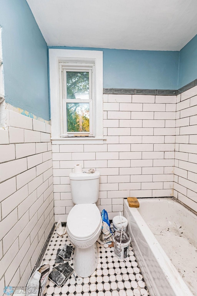 bathroom with a bath, tile patterned flooring, tile walls, and toilet