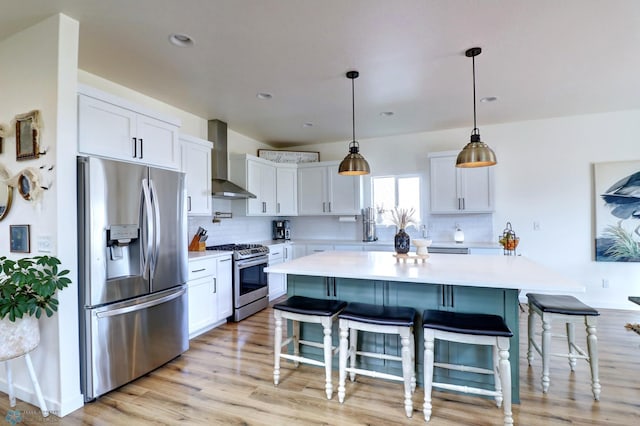 kitchen featuring white cabinets, appliances with stainless steel finishes, wall chimney exhaust hood, and a kitchen bar