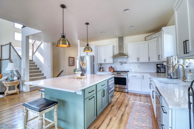 kitchen featuring a kitchen island, light wood-type flooring, stainless steel appliances, white cabinets, and wall chimney exhaust hood