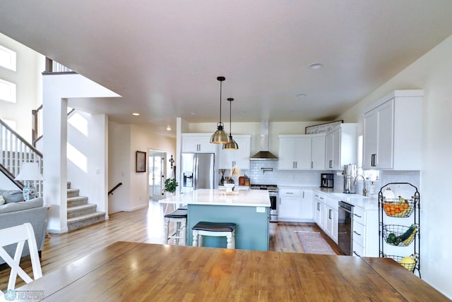 kitchen with a center island, stainless steel appliances, wall chimney range hood, white cabinetry, and hanging light fixtures