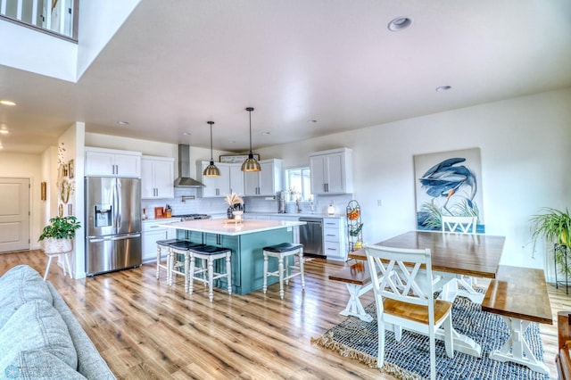 kitchen with a center island, stainless steel appliances, white cabinets, wall chimney range hood, and a kitchen breakfast bar