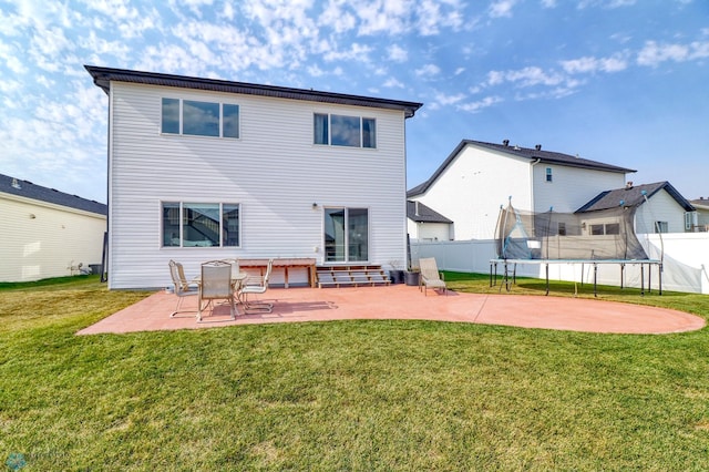 back of property with a trampoline, a patio area, and a lawn