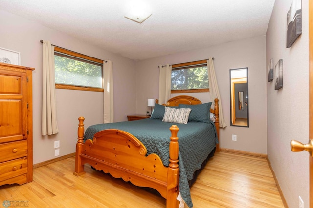 bedroom with a textured ceiling, multiple windows, and light hardwood / wood-style flooring