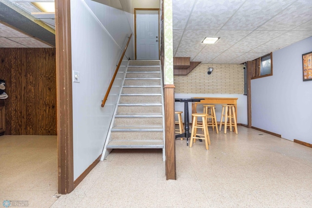 stairs with wooden walls and a drop ceiling