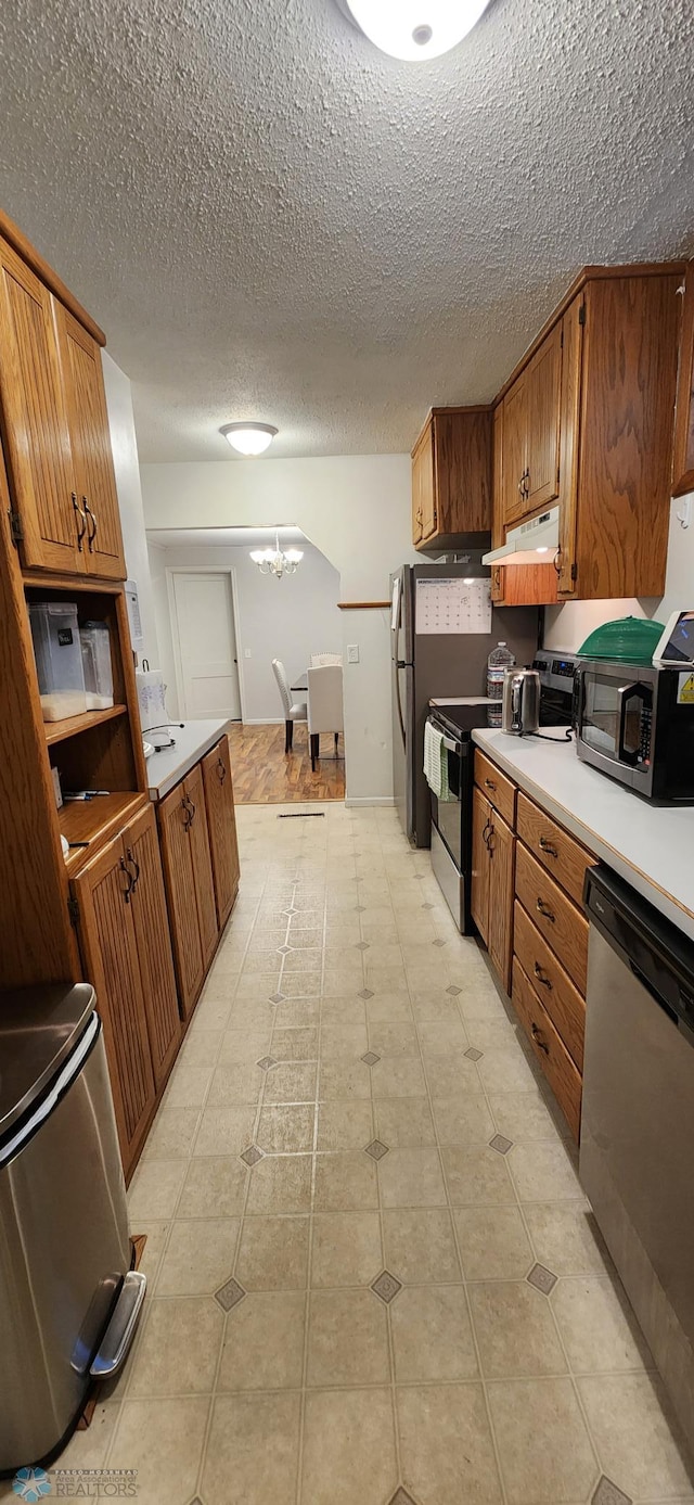 kitchen featuring a textured ceiling, stainless steel appliances, a chandelier, and light tile patterned flooring