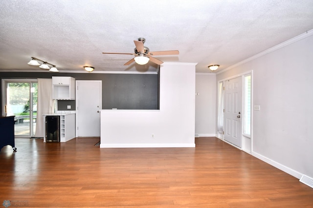 unfurnished living room featuring crown molding, ceiling fan, wood-type flooring, and a textured ceiling