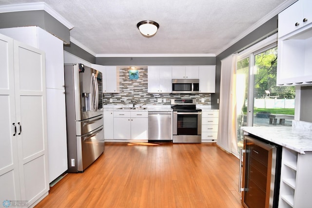 kitchen featuring stainless steel appliances, white cabinets, beverage cooler, light hardwood / wood-style floors, and ornamental molding