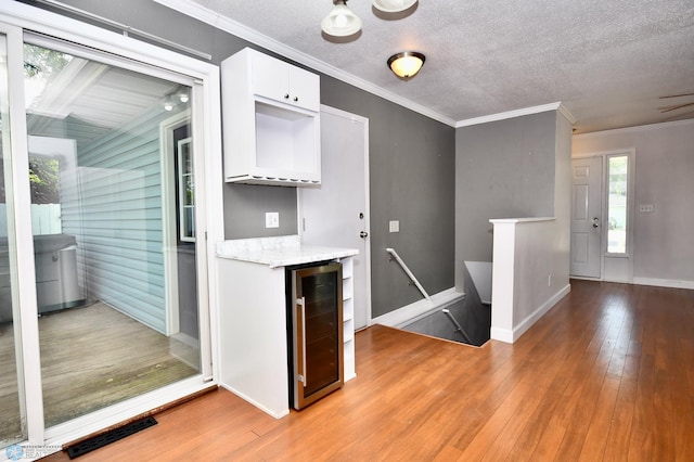 kitchen featuring light wood-type flooring, white cabinets, beverage cooler, crown molding, and a textured ceiling