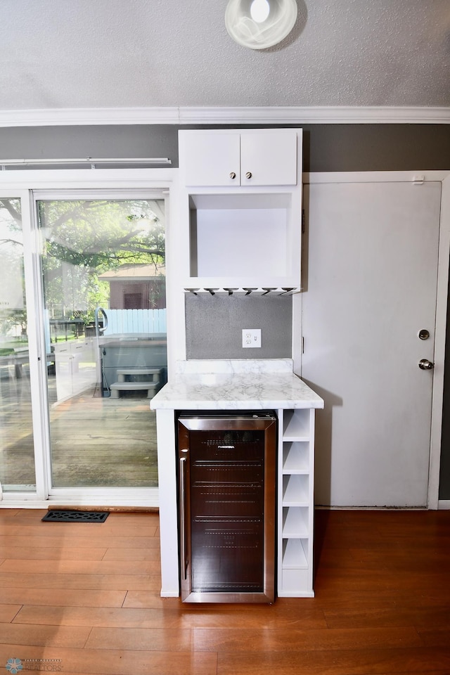 bar with hardwood / wood-style flooring, beverage cooler, white cabinets, and a textured ceiling