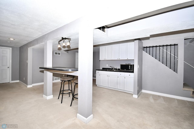 kitchen featuring white cabinets, light carpet, sink, a breakfast bar area, and a textured ceiling