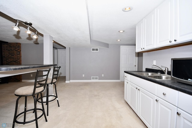 kitchen with light colored carpet, sink, a kitchen breakfast bar, and white cabinets