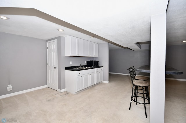 kitchen featuring light carpet, sink, a breakfast bar, and white cabinets