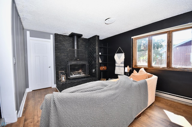 bedroom featuring a wood stove, baseboard heating, hardwood / wood-style flooring, and a textured ceiling