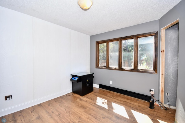 unfurnished room featuring a baseboard radiator, light wood-type flooring, and a textured ceiling